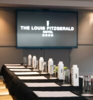 Elegant conference room setup at Louis Fitzgerald Hotel, featuring a screen and meeting materials.