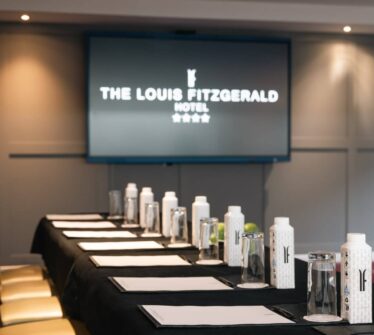 Elegant conference room setup at Louis Fitzgerald Hotel, featuring a screen and meeting materials.