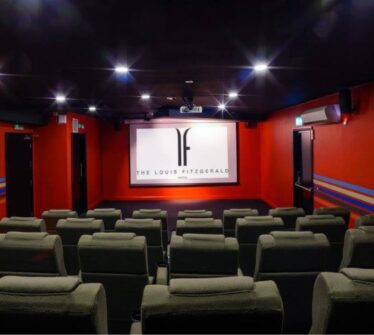 Comfortable theatre room at Louis Fitzgerald Hotel with plush seats and dim lighting.