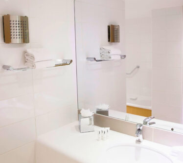 Modern hotel bathroom with shower, white towels, and toiletries on a vanity.