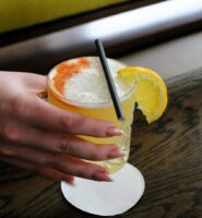 A hand holding a fruity cocktail on a wooden table at Louis Fitzgerald Hotel.