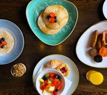A luxurious breakfast spread at Louis Fitzgerald Hotel featuring pancakes, a cooked breakfast, and fresh fruits.