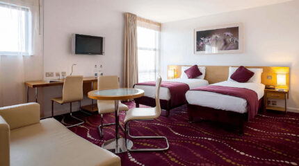 Elegant hotel room with twin beds, plush purple accents, and natural light at Louis Fitzgerald.