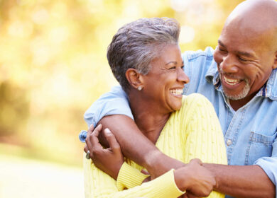 Older couple smiling and embracing warmly outdoors in a sunlit park.