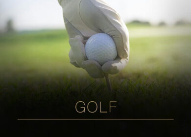 A hand in a glove places a golf ball on a tee on a lush green course. Text reads "GOLF.