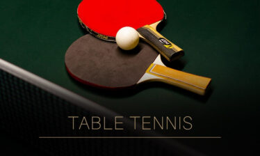 Two table tennis paddles and a ball on a green table.