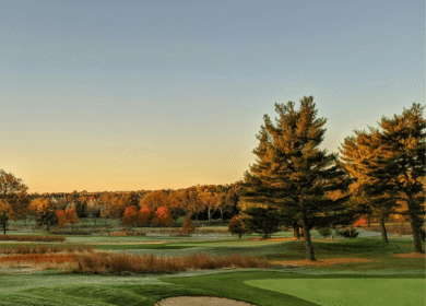 Scenic golf course at sunset with lush green fairway and surrounding autumn trees.