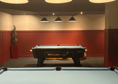 Cosy hotel game room with pool tables under warm lighting.