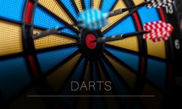 Close-up of darts hitting a colourful dartboard at Louis Fitzgerald Hotel. Text reads "Darts".