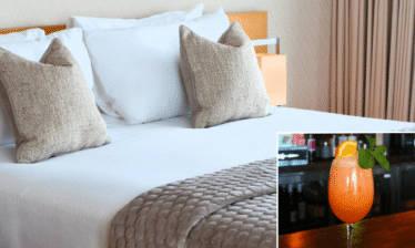 Elegant hotel room with plush bedding and a refreshing cocktail on a bar counter.