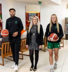 Three people standing indoors at Louis Fitzgerald Hotel, two holding basketballs.