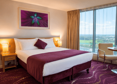 Elegant hotel room with cosy bed and large window view.