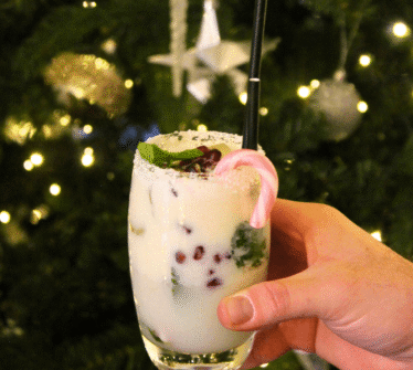 Festive cocktail held by a hand in front of a decorated Christmas tree.