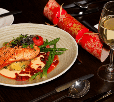 Gourmet salmon dish with asparagus served on a set restaurant table with a glass of white wine.