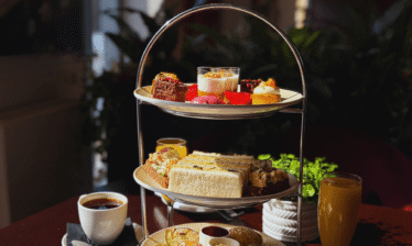 Elegant afternoon tea setup with sandwiches, pastries, and drinks at Louis Fitzgerald Hotel.