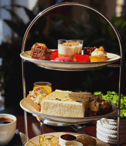 Elegant afternoon tea setup with sandwiches, pastries, and drinks at Louis Fitzgerald Hotel.