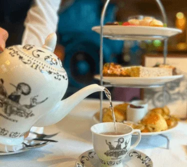 Hotel staff pouring tea in elegant dining setting with tiered tray of pastries.