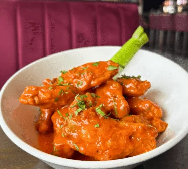 Bowl of spicy buffalo wings garnished with fresh herbs in a cosy restaurant setting.