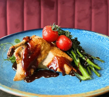 Succulent chicken dish with tomatoes and greens on a blue plate at a luxury Dublin hotel.