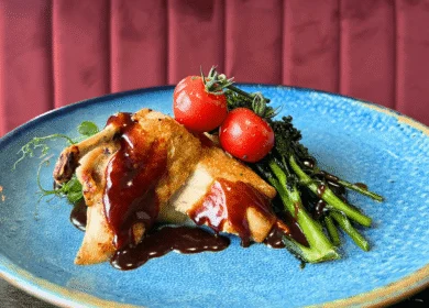 Succulent chicken dish with tomatoes and greens on a blue plate at a luxury Dublin hotel.