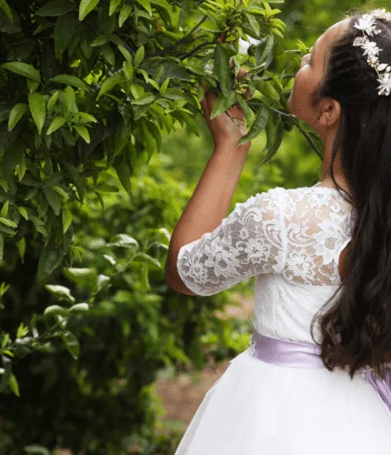 Young girl in white dress with flower crown surrounded by lush greenery at a hotel garden.