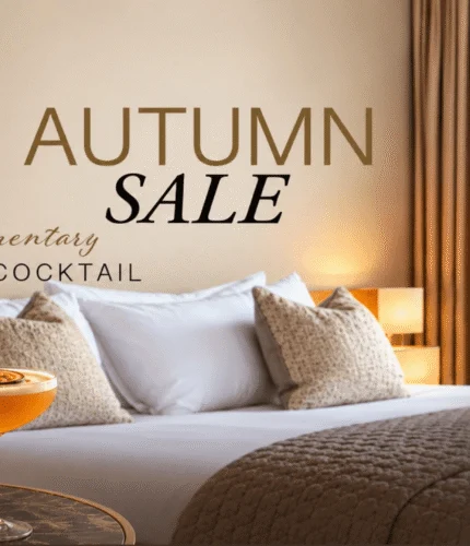 Elegant hotel room with king bed, autumn leaves view, and cocktail on the table.