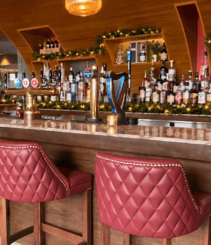 Cosy hotel bar with festive decorations and red cushioned stools.