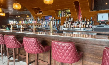 Modern hotel bar with red quilted stools and a variety of drinks on display.
