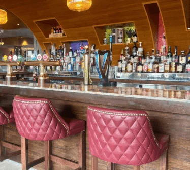 Modern hotel bar with red quilted stools and a variety of drinks on display.
