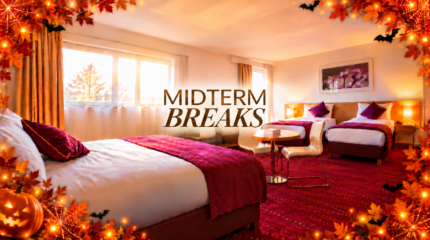 Bright twin/double hotel room with warm autumn decor, three beds, table and chairs, and "MIDTERM BREAKS" text