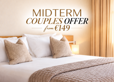 Bright cosy hotel double bed with cushions, soft quilt and wall text "MIDTERM COUPLES OFFER from €149" in warm Dublin hotel room, inviting stay (80 characters)