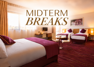 Bright twin-room at Louis Fitzgerald Hotel with cosy beds, desk, seating area and "MIDTERM BREAKS" text
