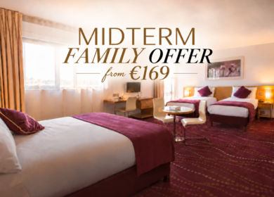 Spacious family hotel room with three beds, warm lighting, desk, seating and "MIDTERM FAMILY OFFER from €169" text visible